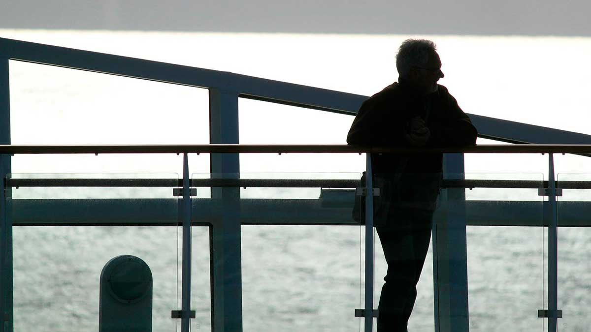 image of a man standing by a railing in front of a dull sky with more light visible behind him than on him