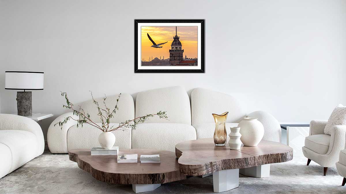 Picture frame featuring a photo of a bird flying in the sunset with the city behind hung in a modern living room